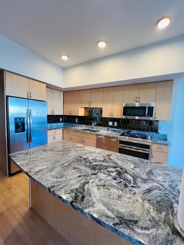 kitchen with appliances with stainless steel finishes, light brown cabinetry, sink, stone countertops, and light hardwood / wood-style flooring