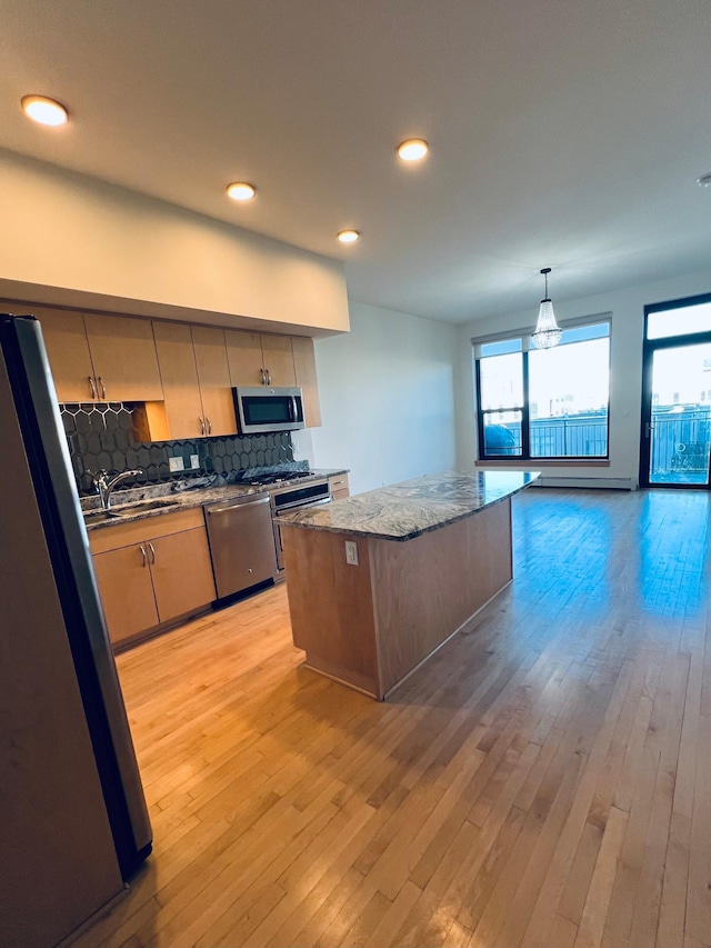 kitchen with appliances with stainless steel finishes, light wood-type flooring, backsplash, sink, and a center island