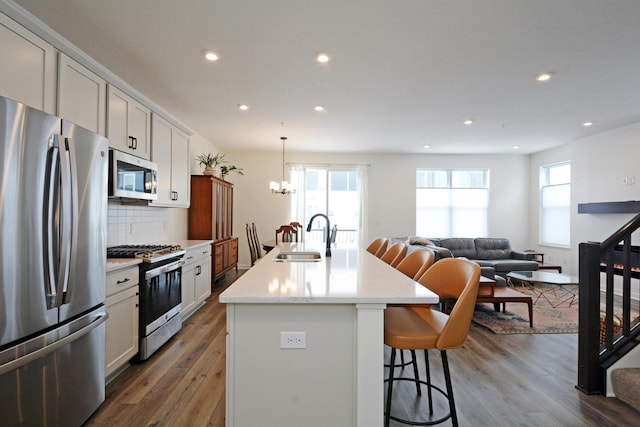 kitchen featuring appliances with stainless steel finishes, sink, backsplash, a kitchen island with sink, and a breakfast bar