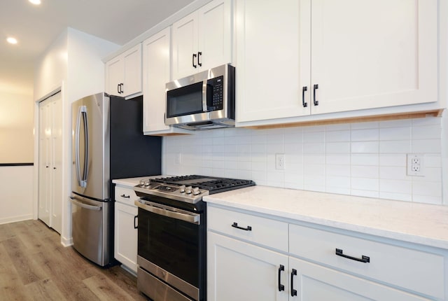 kitchen with tasteful backsplash, light hardwood / wood-style floors, light stone countertops, appliances with stainless steel finishes, and white cabinets