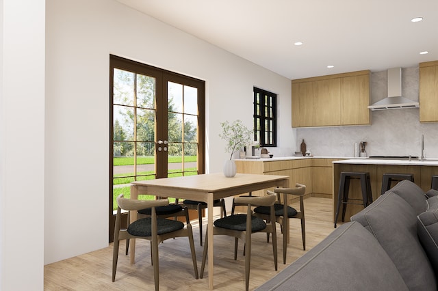 kitchen featuring french doors, wall chimney exhaust hood, tasteful backsplash, light brown cabinetry, and light wood-type flooring