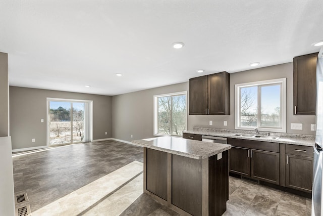 kitchen featuring sink, a center island, dark brown cabinetry, light stone counters, and stainless steel dishwasher