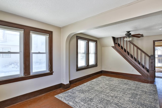 interior space with a textured ceiling, ceiling fan, dark wood-type flooring, baseboards, and stairs