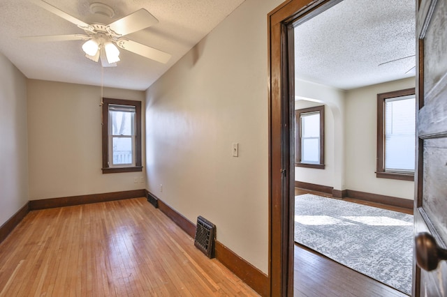 spare room featuring a textured ceiling, light wood-type flooring, a wealth of natural light, and baseboards