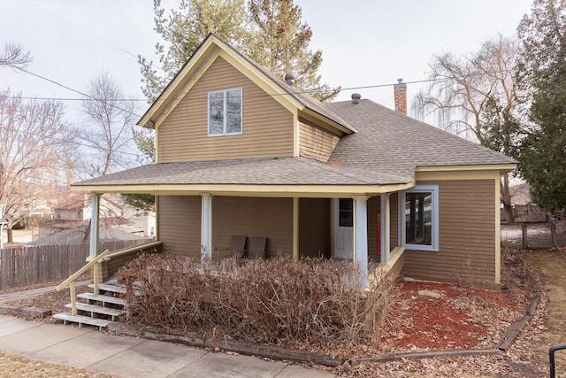 view of front of home with covered porch, roof with shingles, a chimney, and fence