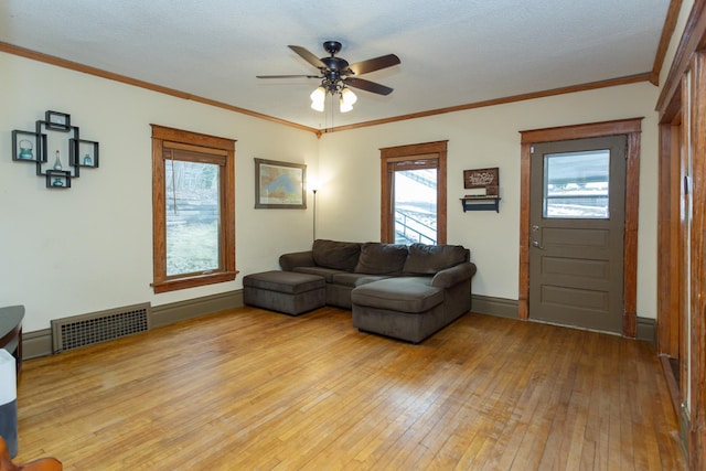 living area featuring visible vents, light wood-style flooring, ornamental molding, baseboards, and ceiling fan