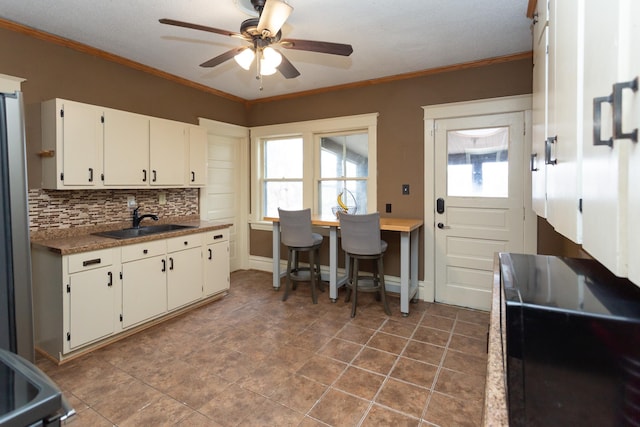 kitchen featuring backsplash, crown molding, ceiling fan, white cabinetry, and a sink