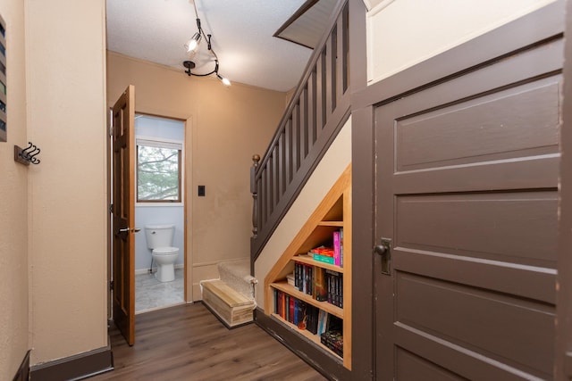 staircase featuring track lighting, a textured ceiling, baseboards, and wood finished floors