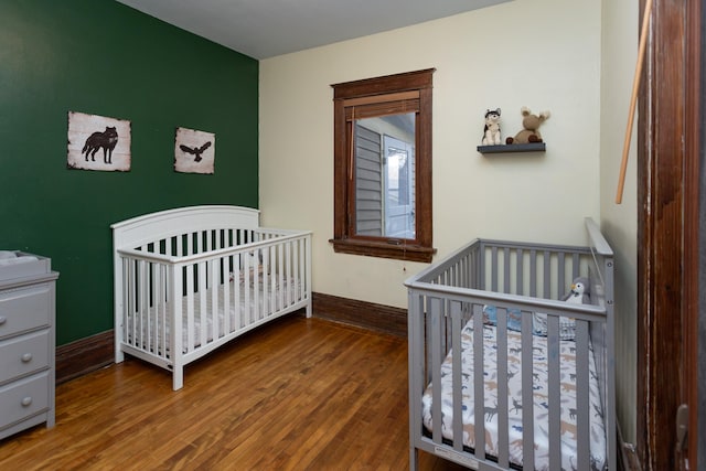 bedroom with baseboards, wood-type flooring, and a crib