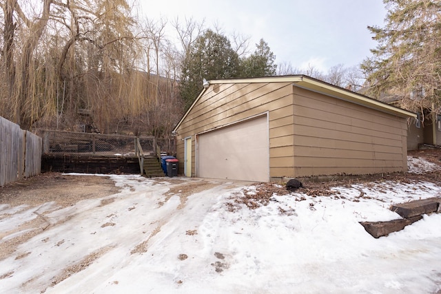 snow covered garage with a detached garage and fence