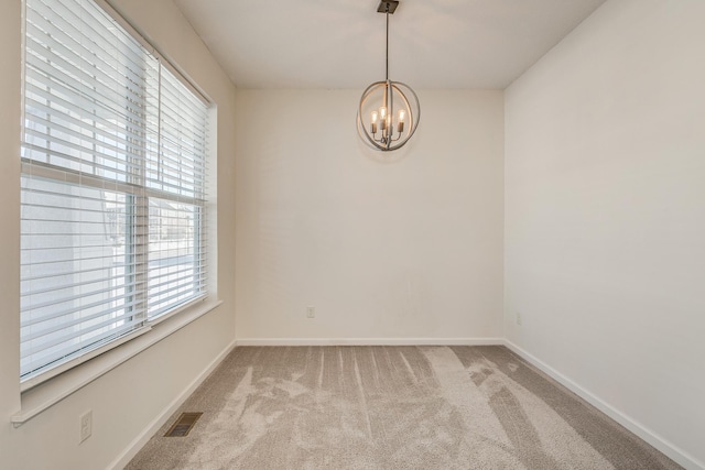 carpeted spare room featuring an inviting chandelier and plenty of natural light