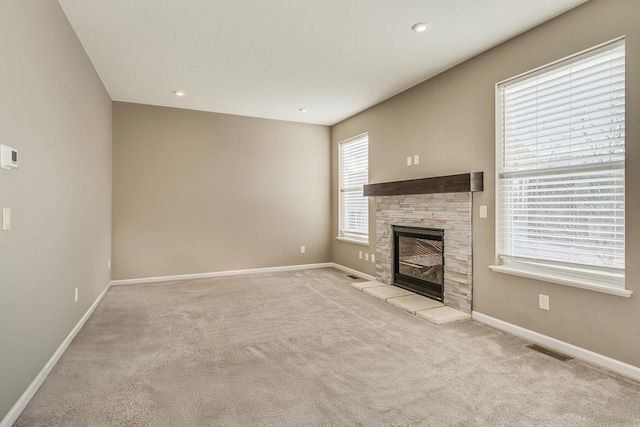 unfurnished living room featuring a healthy amount of sunlight, light colored carpet, and a stone fireplace