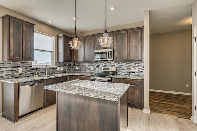 kitchen featuring pendant lighting, a center island, appliances with stainless steel finishes, dark brown cabinets, and sink