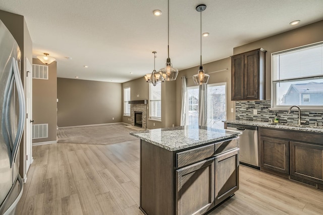 kitchen featuring light stone counters, a center island, sink, stainless steel appliances, and dark brown cabinetry