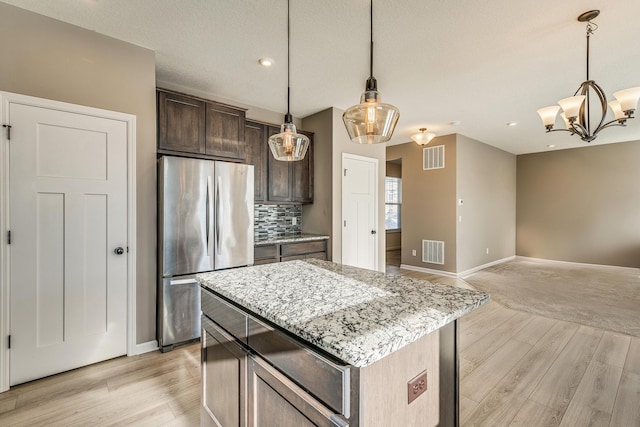 kitchen with hanging light fixtures, tasteful backsplash, a kitchen island, stainless steel refrigerator, and dark brown cabinetry