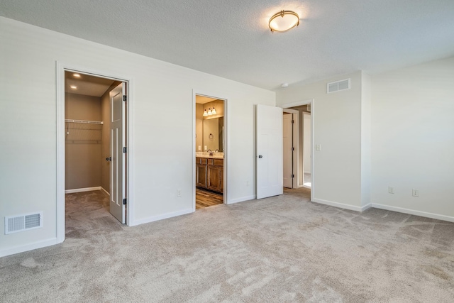 unfurnished bedroom featuring a spacious closet, connected bathroom, a closet, and light carpet