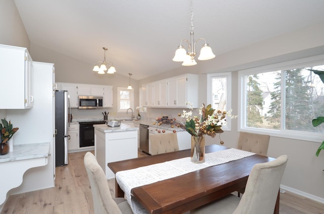 dining space featuring sink, a chandelier, vaulted ceiling, and light hardwood / wood-style floors