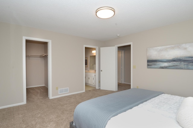 bedroom with a closet, a spacious closet, ensuite bath, and light colored carpet