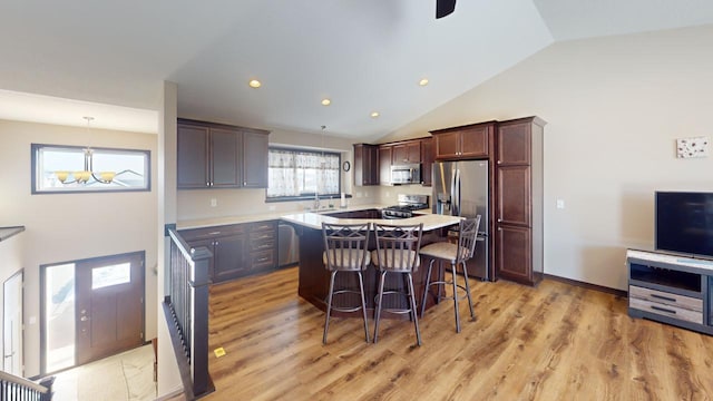 kitchen with light wood-style flooring, appliances with stainless steel finishes, a center island, light countertops, and a kitchen bar