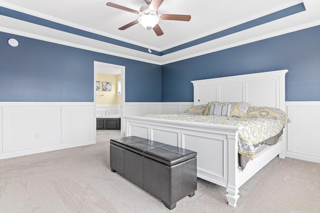 carpeted bedroom featuring a raised ceiling, connected bathroom, crown molding, and ceiling fan