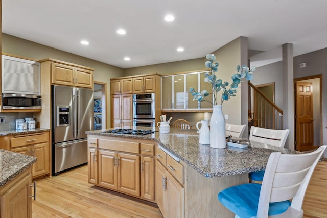 kitchen with a kitchen breakfast bar, light hardwood / wood-style flooring, appliances with stainless steel finishes, light stone countertops, and a kitchen island