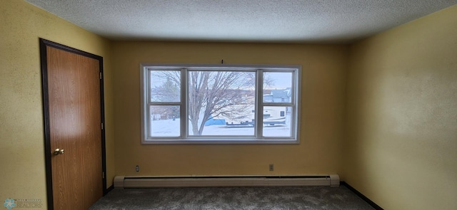 empty room featuring dark colored carpet, a textured ceiling, and a baseboard heating unit