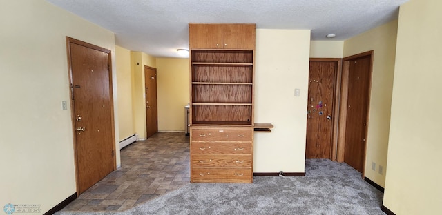 interior space featuring a textured ceiling, dark carpet, and a baseboard heating unit