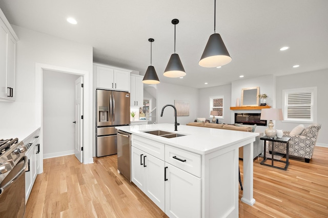 kitchen with white cabinets, appliances with stainless steel finishes, decorative light fixtures, an island with sink, and sink