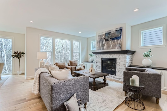 living room featuring a healthy amount of sunlight, a stone fireplace, and light hardwood / wood-style flooring