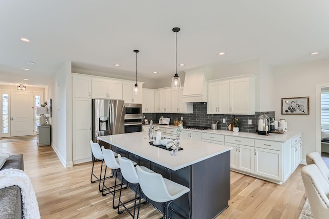 kitchen featuring custom exhaust hood, white cabinets, a kitchen breakfast bar, appliances with stainless steel finishes, and decorative light fixtures