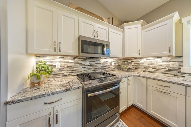 kitchen featuring appliances with stainless steel finishes, tasteful backsplash, light stone counters, vaulted ceiling, and white cabinets