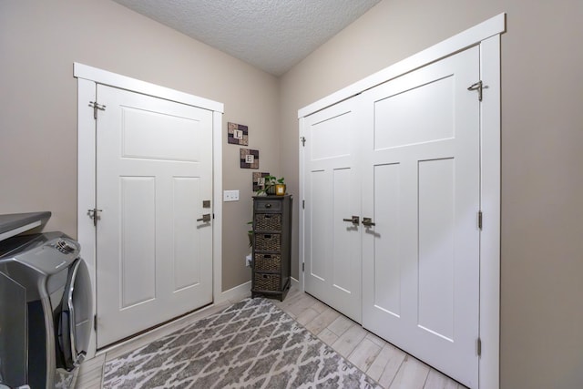 foyer entrance with independent washer and dryer, light wood-type flooring, and a textured ceiling