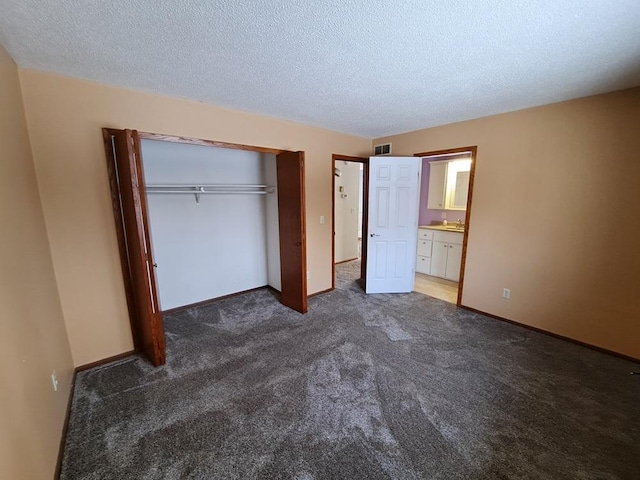 unfurnished bedroom featuring dark colored carpet, ensuite bathroom, a textured ceiling, and a closet