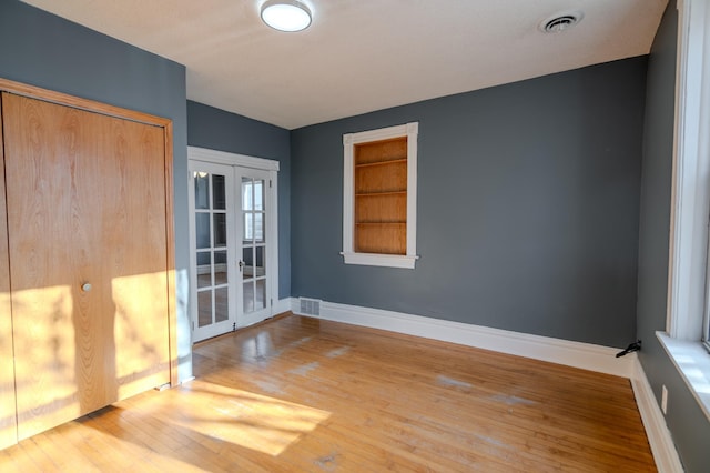 spare room featuring french doors, hardwood / wood-style flooring, and built in shelves