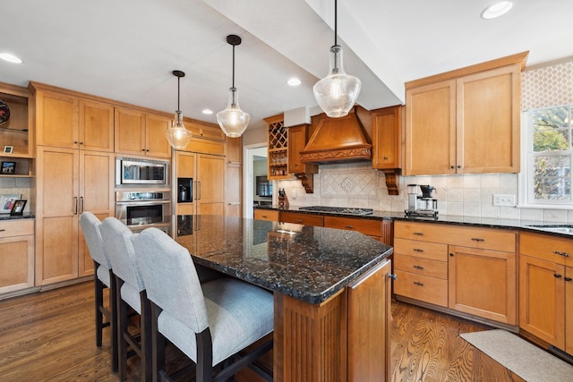 kitchen with hanging light fixtures, stainless steel appliances, a kitchen island, custom range hood, and a kitchen breakfast bar