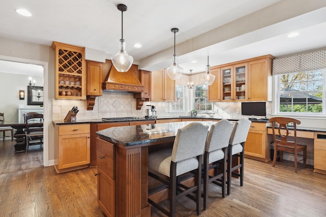 kitchen with dark stone countertops, a center island, premium range hood, decorative light fixtures, and dark hardwood / wood-style flooring