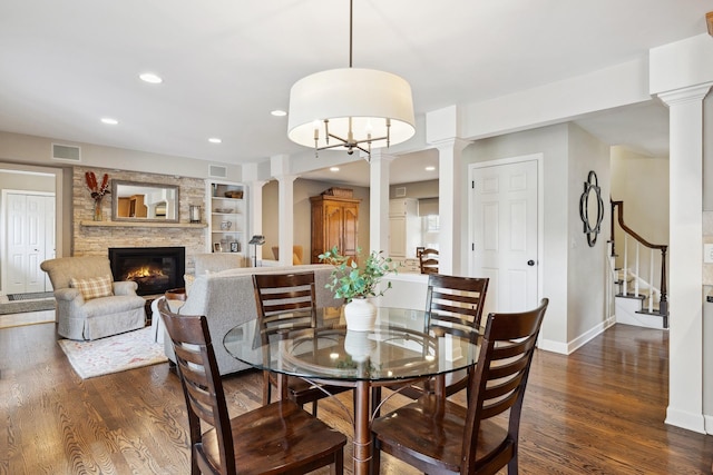 dining room featuring dark hardwood / wood-style flooring, a stone fireplace, decorative columns, and built in shelves