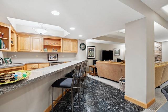 kitchen featuring light brown cabinetry, dishwasher, a tray ceiling, sink, and a kitchen bar