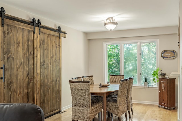 dining room with a barn door, a healthy amount of sunlight, and light wood-type flooring