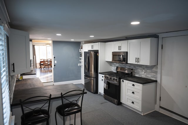 kitchen with stainless steel appliances, white cabinetry, a kitchen bar, and backsplash