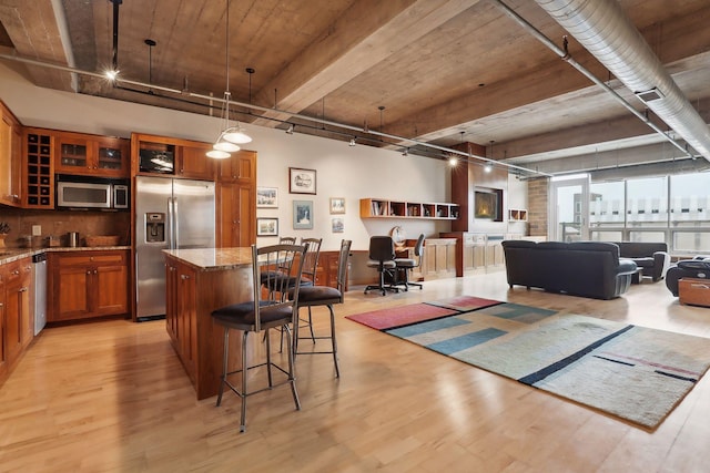 kitchen with hanging light fixtures, a breakfast bar area, a kitchen island, light stone counters, and stainless steel appliances