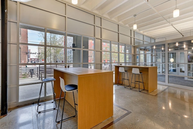 bar with a wealth of natural light, a towering ceiling, decorative light fixtures, and a wall of windows