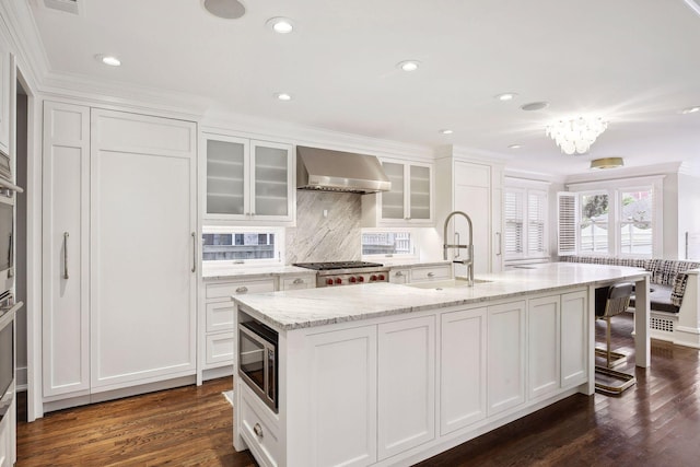 kitchen featuring white cabinets, a kitchen island with sink, wall chimney range hood, and sink