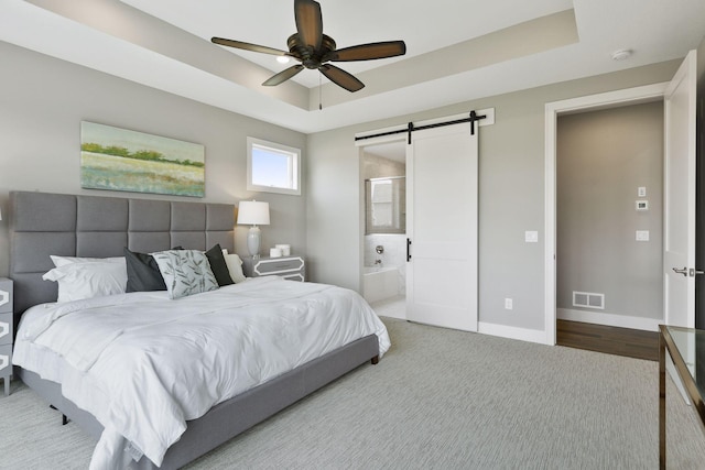 bedroom featuring a raised ceiling, ensuite bath, ceiling fan, and a barn door