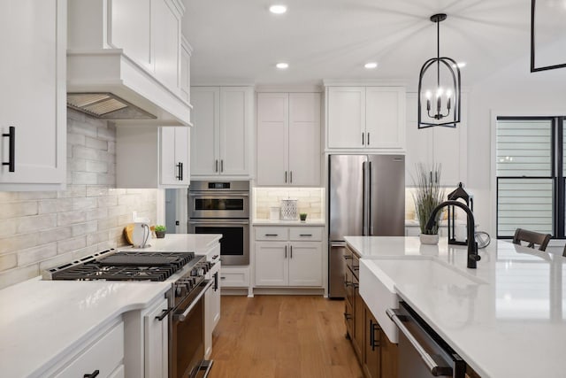 kitchen with premium appliances, white cabinetry, sink, hanging light fixtures, and light wood-type flooring