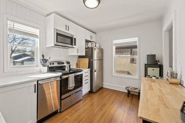 kitchen with light hardwood / wood-style floors, ornamental molding, backsplash, appliances with stainless steel finishes, and white cabinets