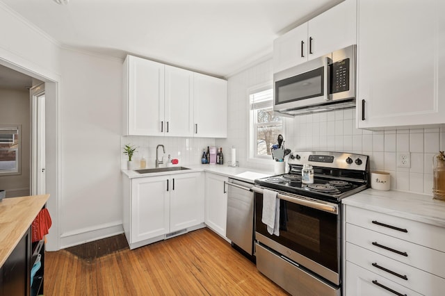 kitchen featuring appliances with stainless steel finishes, sink, light wood-type flooring, white cabinets, and tasteful backsplash