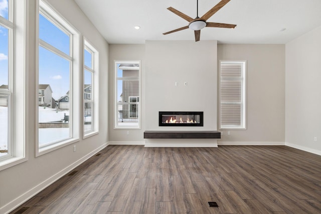 unfurnished living room with ceiling fan, dark wood-type flooring, and a healthy amount of sunlight