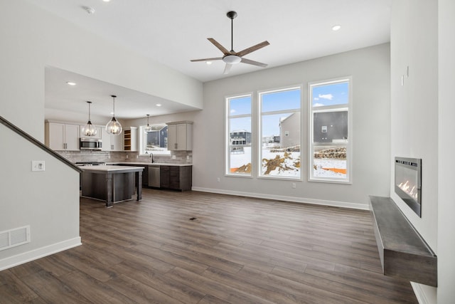 unfurnished living room featuring heating unit, sink, dark wood-type flooring, and ceiling fan