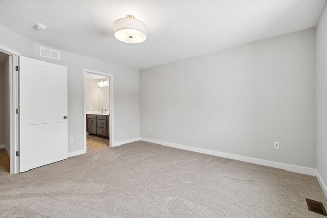 unfurnished bedroom with light carpet, a textured ceiling, and ensuite bathroom